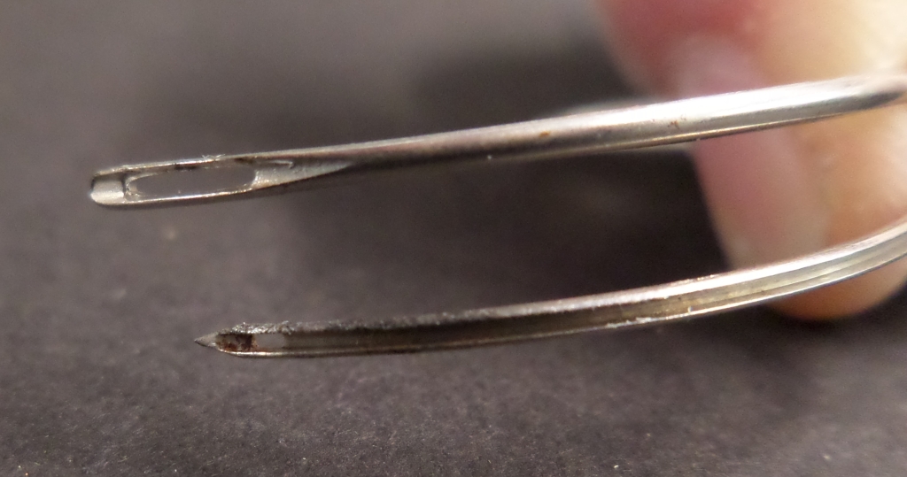 Close up comparing modern bookbinding needle (top) with old-style curved needle (bottom)